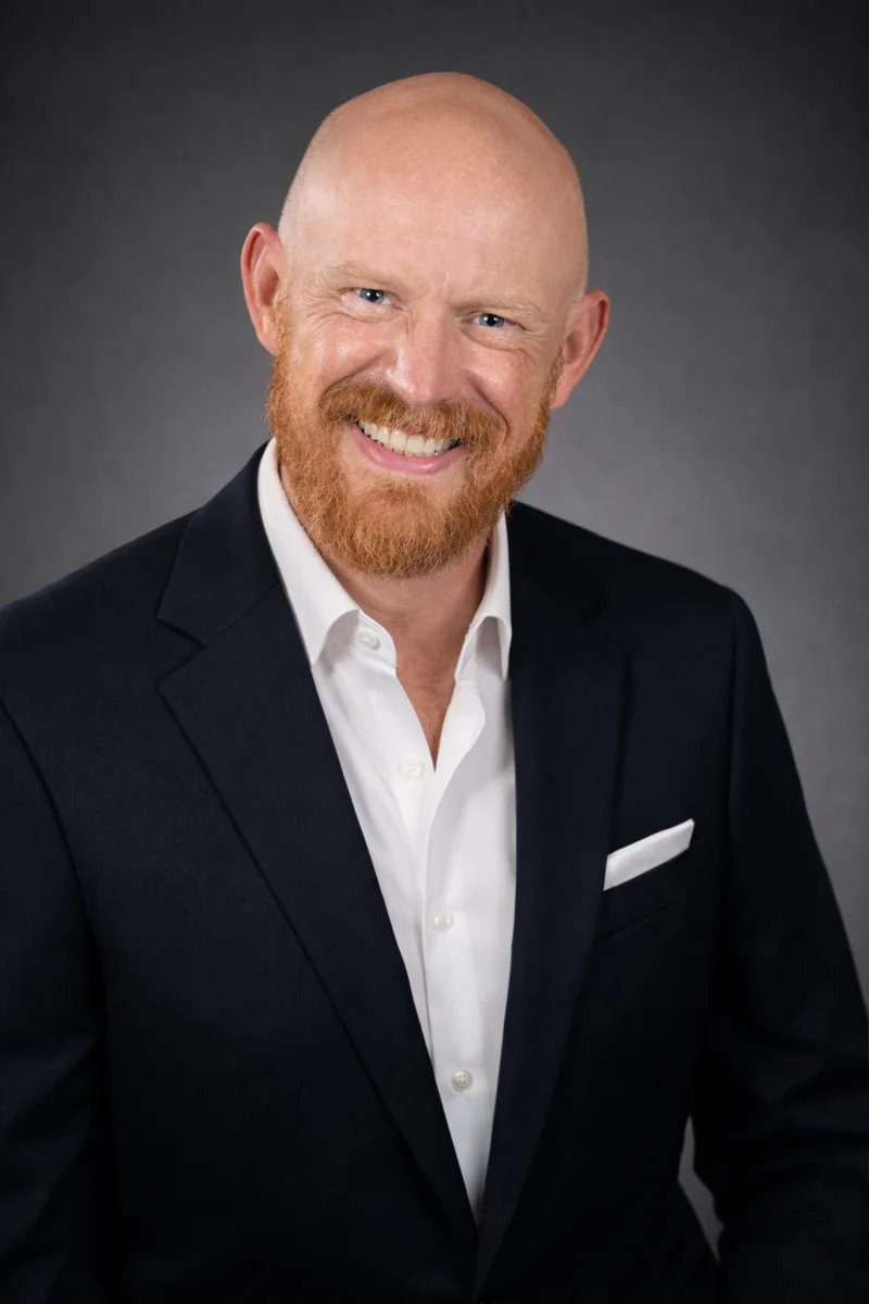 Rick Byrne smiling in a dark jacket and white shirt